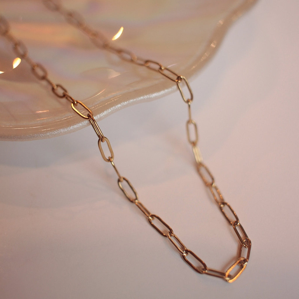 Gold chain necklace on a white surface with a blurred background