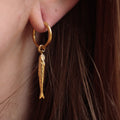 Gold hoop earring with a fish charm worn by a person.